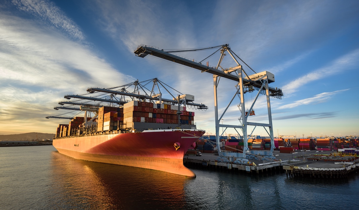 Low Angle Aerial Shot of Cranes Looming Over Container Ship