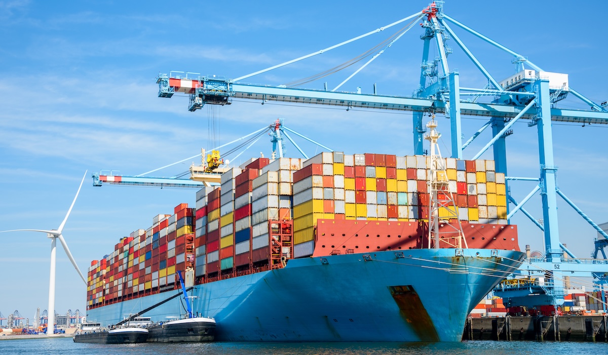 Un inmenso buque de carga, repleto de contenedores, amarrado en una terminal portuaria un soleado día de verano